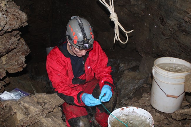 Person in a cave next to two buckets.