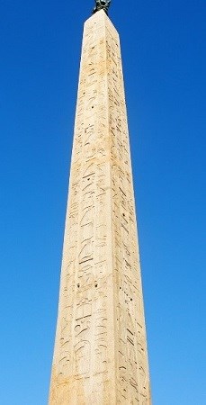 single white obelisk with carvings against a blue sky.