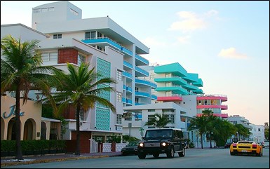 View from street of art deco white buildings with turquoise, pastel blue, or pink trim.