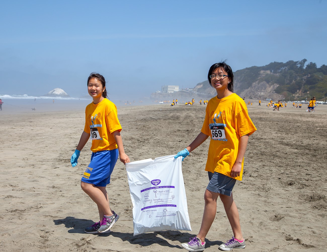 Two girls holding a trash bag walking on the ocean beach