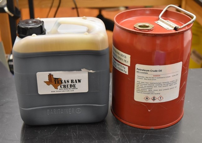 Oils in containers - West Texas Intermediate and Access Western Winter Two types of oil jugs next to each other, one in a cylinder metal container and the other in a plastice one