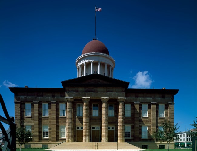Color Photo of stone Illinois Capitol building with massive Doric columns and brown-clad dome surmounted by a flagpole and US flag