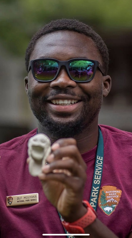 Olf smiling to the camera holding a small sculpture of a person with an open mouth made out of rock