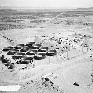 241 T Tank Farm A black and white aerial photo of a desert landscape dotted with industrial buildings and twelve large black circular structures.