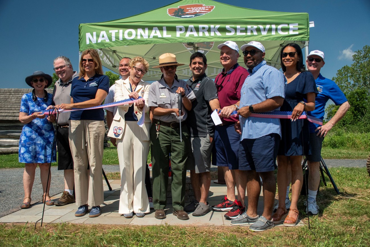 A group of people gather for a photo as they cut a ribbon with large scissors