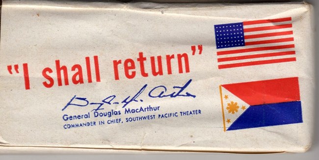 A small, rectangular white paper package printed with the American and Philippine flags. Printed in red: “I shall return.” Below, in blue: the signature of General MacArthur, and “General Douglas MacArthur, Commander in Chief, Southwest Pacific Theater.”
