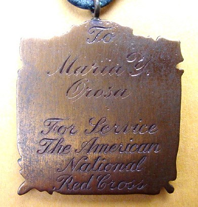 Square metal medal (possibly brass) engraved in a script font.