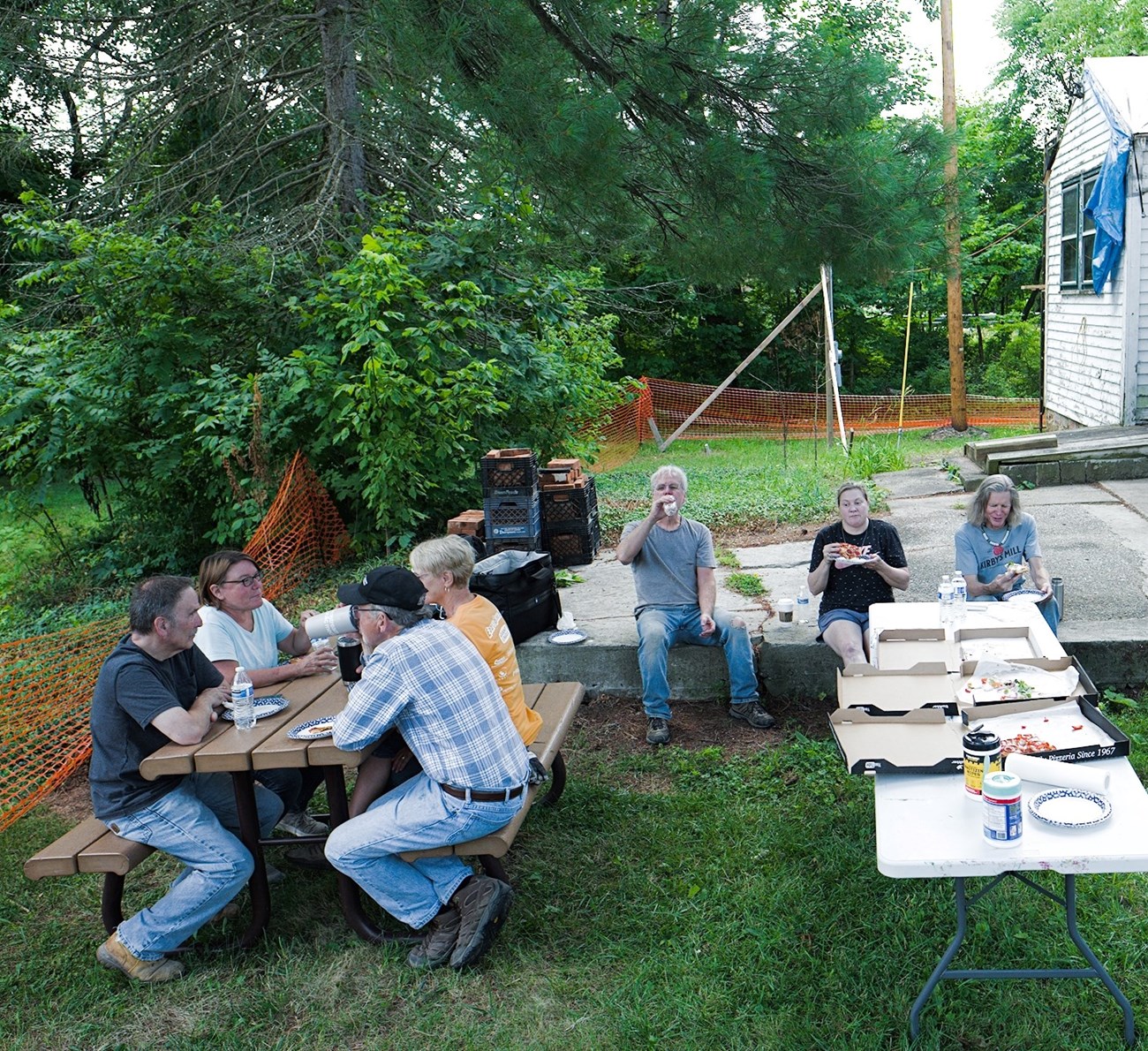 Photograph of seven volunteers taking a pizza break for lunch outside of the house.