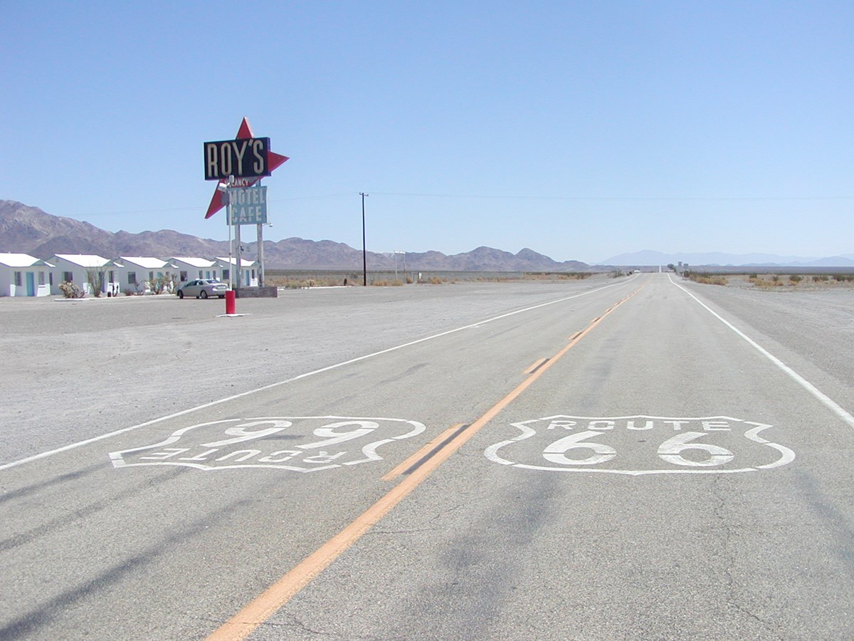 Two white shield emblems painted on a paved road read "Route 66".