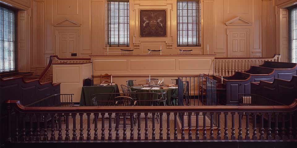 Interior view of a courtroom with judges' bench and jury boxes flanking a lawyers' table.