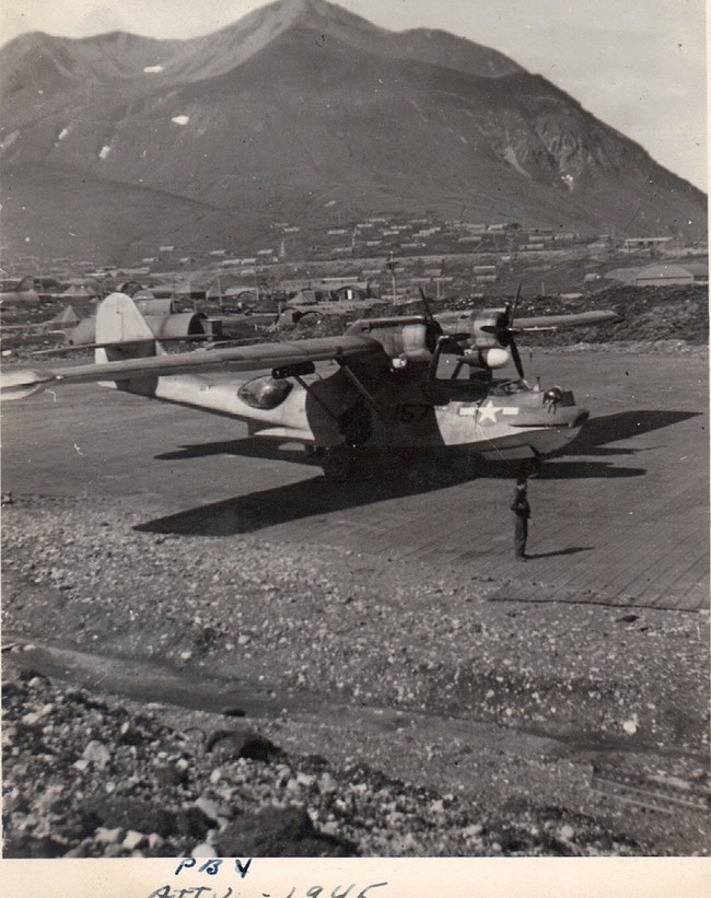 Plane parked on gravel runway with mountains in the distance