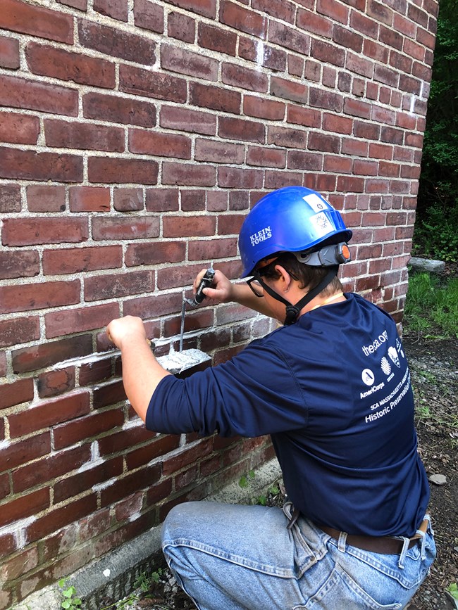 A Historic Preservation corps member wearing a hard hat applying mortar to a brick wall.