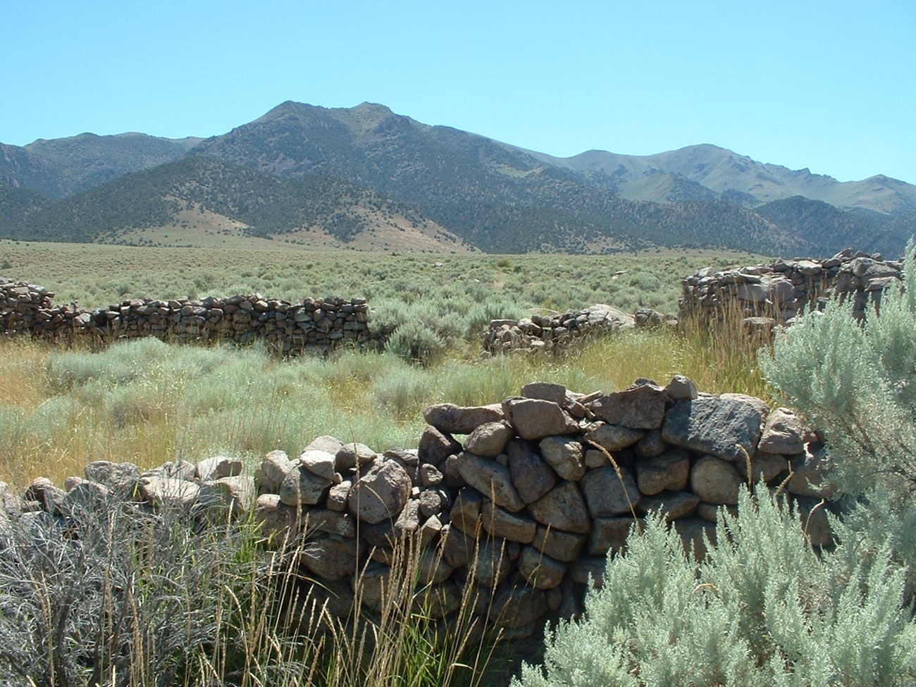 A ruins of a stone wall with distant desert mountains.