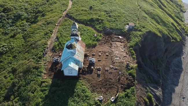 Park Science A white church with a green roof stands 80 feet away from a cliff edge across an expanse of ground.