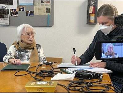Two women sit at a table during a recorded oral history interview.