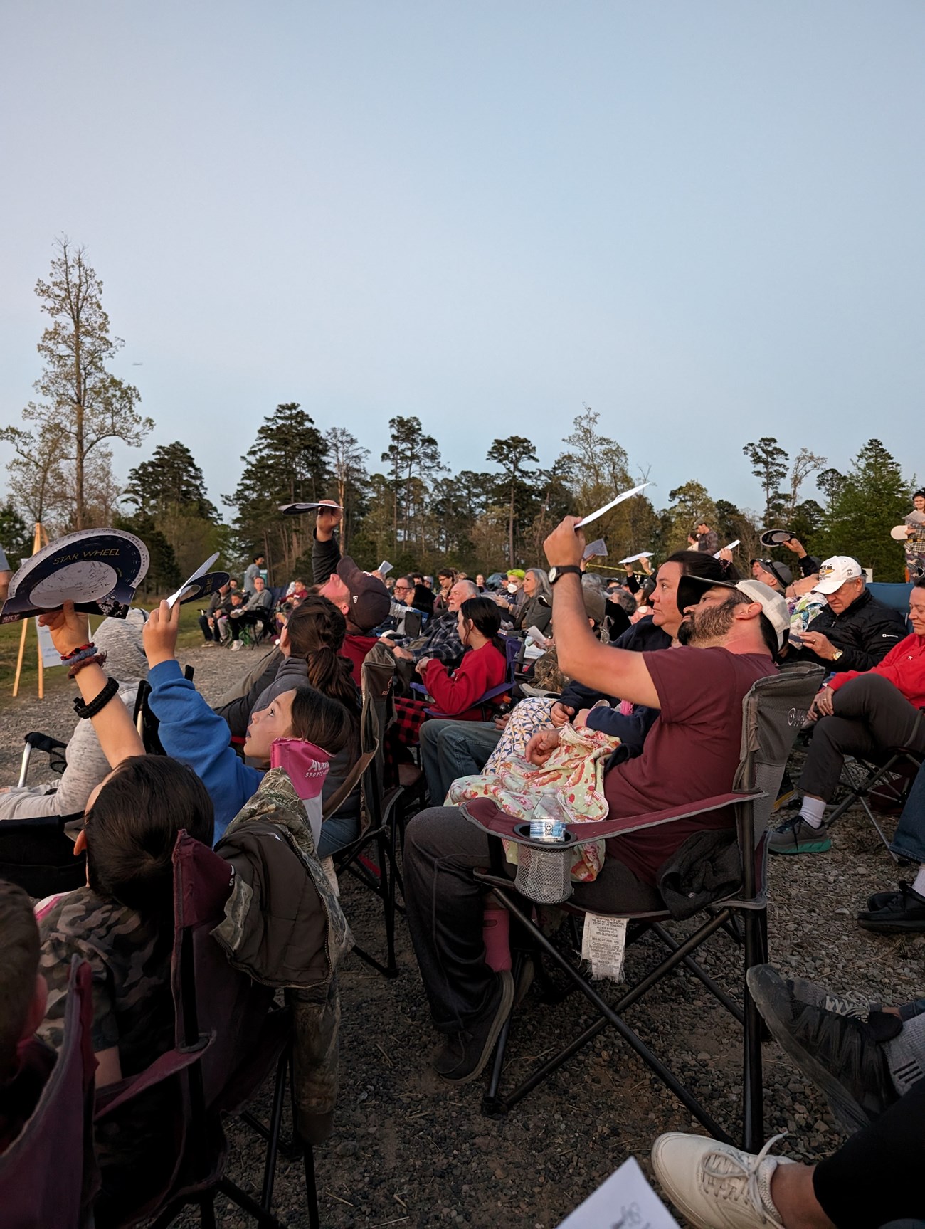 Night Sky Programming A crowd seating in lawn chairs looks up at the twilight sky with a paper celestial maps held in the air.