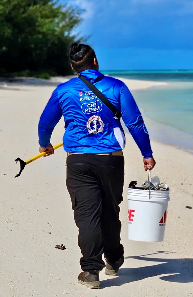 Pacific Islands Conservation Corps intern Isaiah Joel Torre, American Memorial Park Back toward the viewer, an intern carries a bucket and clamp to pick up trash on a beach
