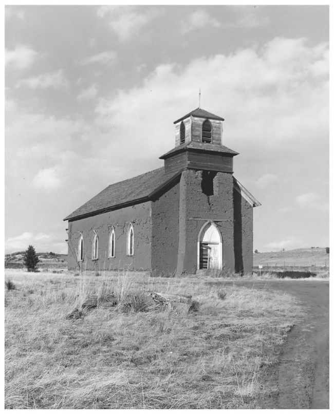 A historic image of a church with one steeple, in a grassy field.