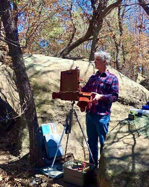 Man standing in wooded area with an easel