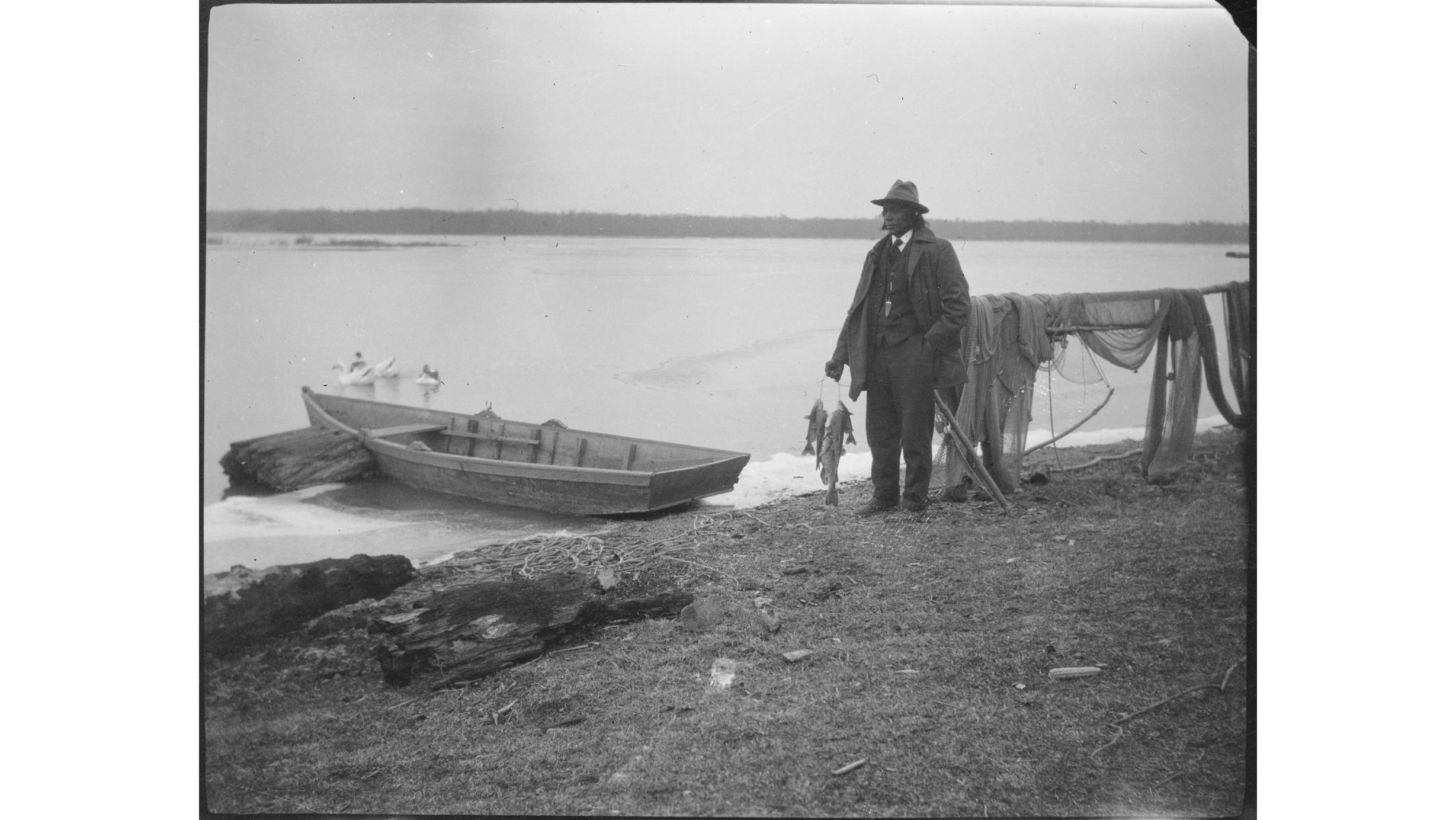 Pamunkey Chief George Major Cook A black and white photograph of a man next to a rowboat and fishing net.