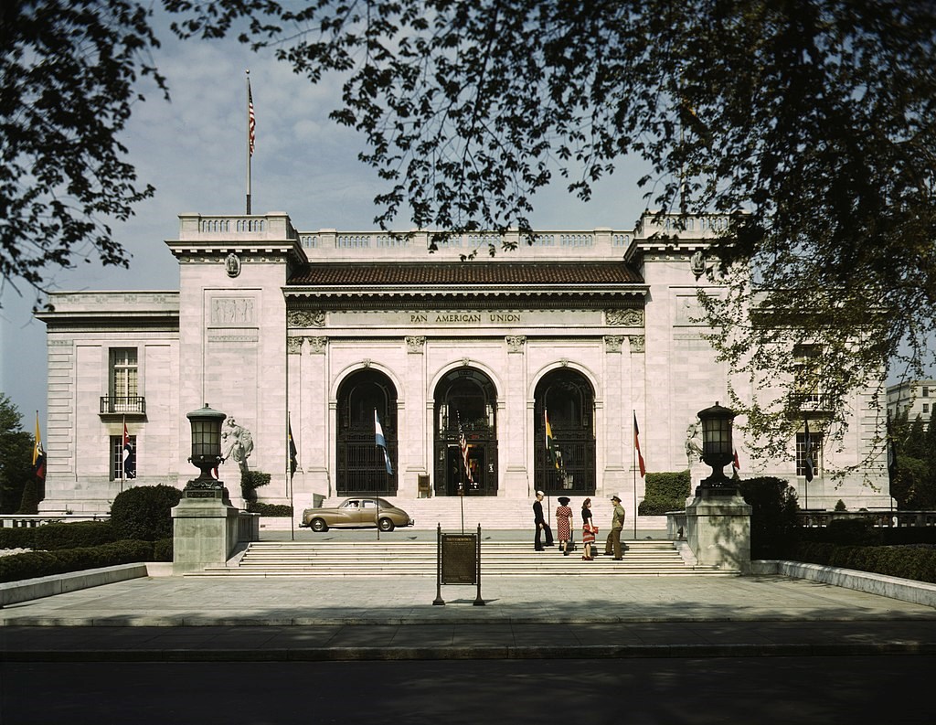 Pan American Headquarters building in Washington, DC, 1943. There are four people walking towards the building and a vintage car.