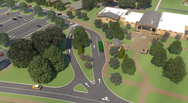 High angle view of an entrance road to a parking lot with divided lanes. A green tour bus is parked near large building while a yellow vehicle uses another lane to drive toward a large parking area in the background with scattered parked cars and trees.