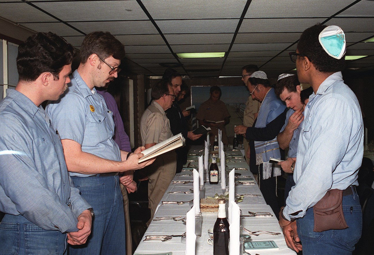 Men standing at a table. Some wear Jewish religious clothing.