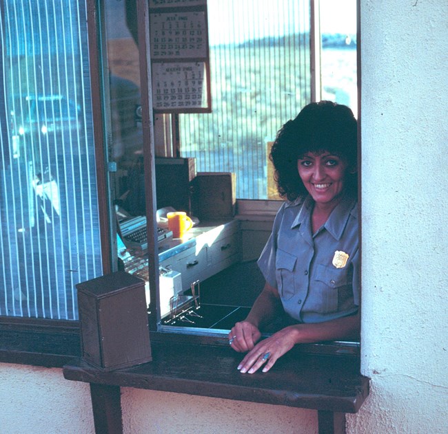 Patsy Otero in her NPS uniform smiles as she sits at the window of an entrance station.
