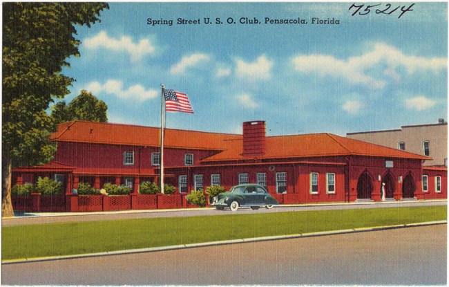 Spring Street USO Colorful postcard of a single story red building with a green lawn, an American flag flying on a pole and a blue sky in the background