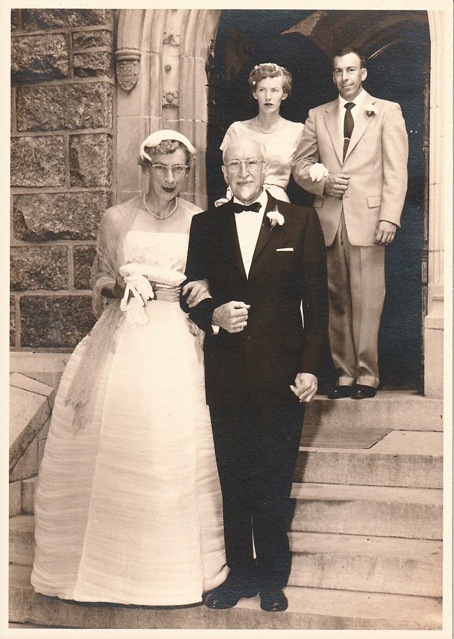 A bride and groom walk out of a doorway followed by two more people
