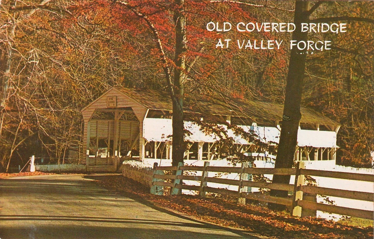 A postcard featuring a wooden covered bridge in fall. The postcard reads " Old Covered Bridge at Valley Forge"