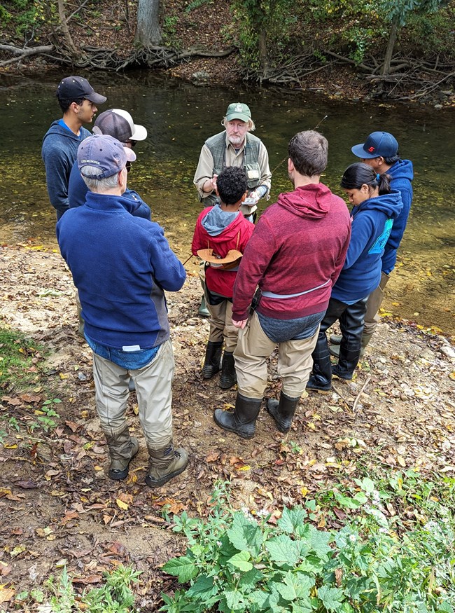 A group of people standing around a volunteer holding a fly fishing pole.