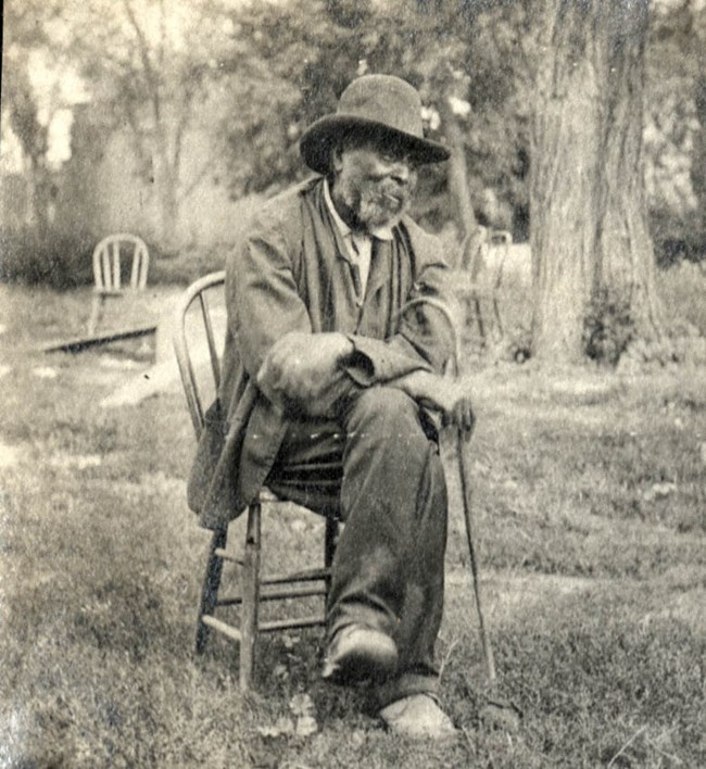 African American man sitting on a chair in an outdoor setting in 1905.