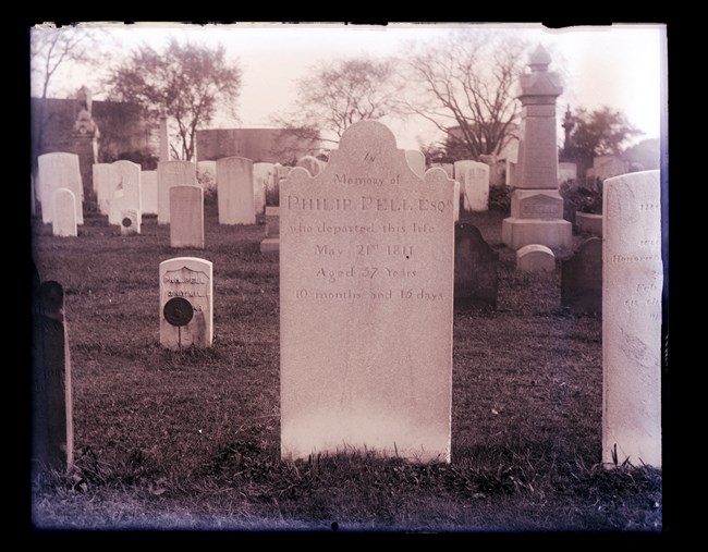 White, vertical gravestone, with letters, in a cemetery, surrounded by other gravestones