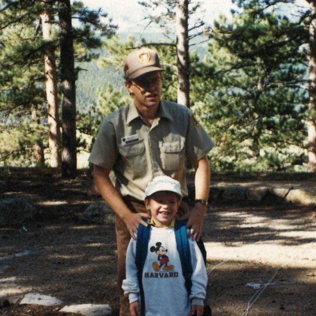 Tom Medema at Rocky Mountain National Park in his volunteer uniform, smiling for the photo with a young kid.