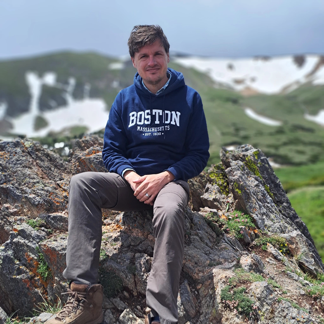 scientist Danny Haelewaters sitting on some rocks wearing a Boston sweatshirt