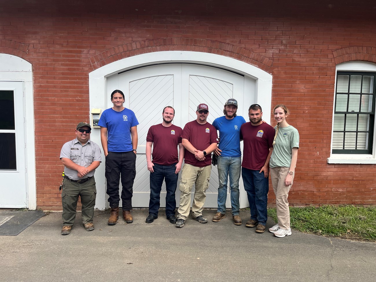 A group of people stand in front of a large curved white door and brick building.