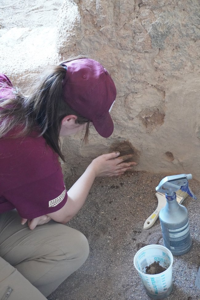 Person applying mortar to a whole in a rock wall with tools by their side