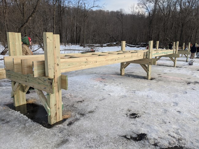 Partially constructed boardwalk over a frozen pond.