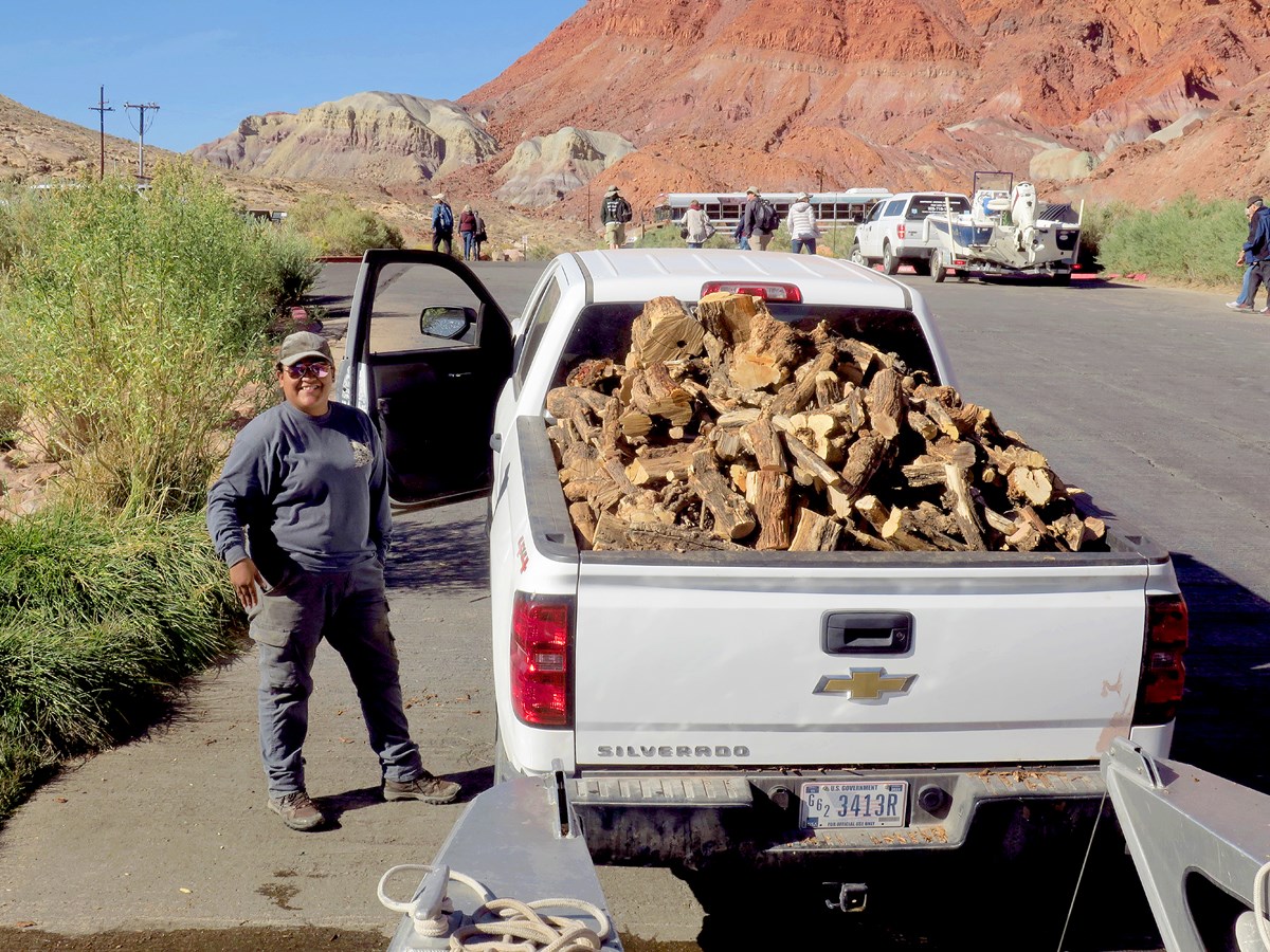 Woman stands next to a white pickup truck with a cord of tamarisk firewood at Lees Ferry