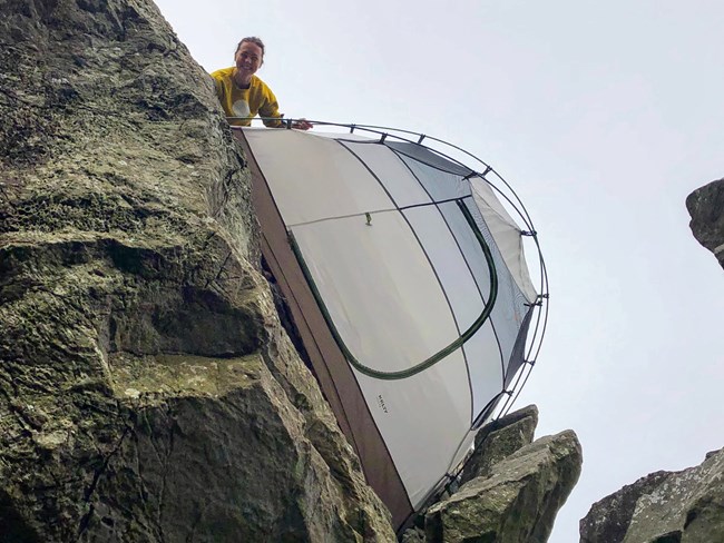 Katherine Stratton Woman holds tent sideways off a rock ledge.