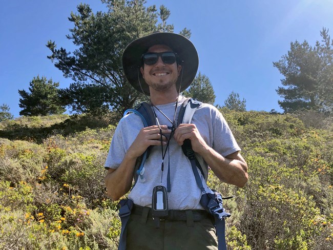 Brett Stormoen Brett smiles in the sun while standing in a dense patch of shrubs.