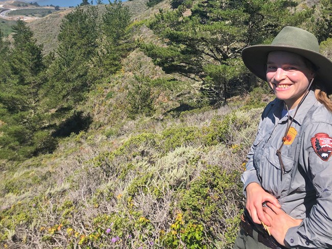 Lisa smiles in the sun while standing in a dense patch of shrubs.