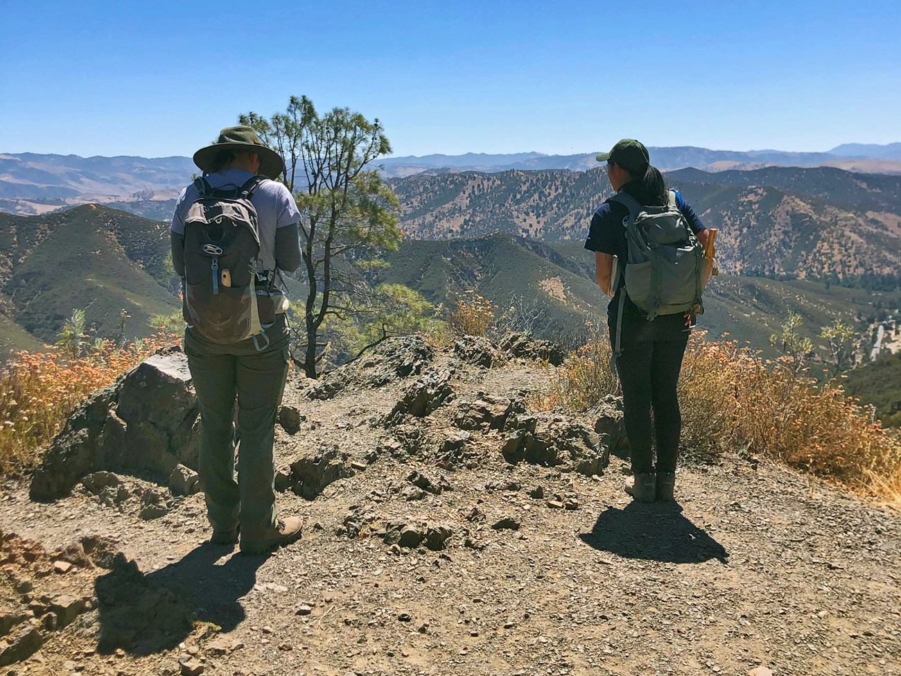 Two women on a rocky outcrop looking out over a hilly landscape.