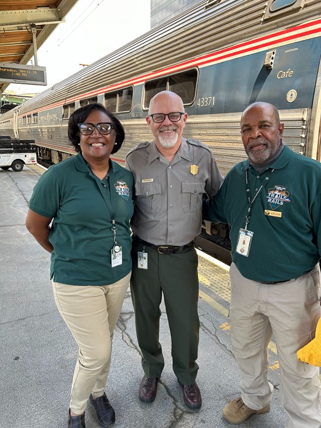 Tom in his ranger uniform standing with volunteers in front of an Amtrak train.