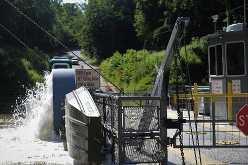 A detail of a vehicle ferry vessel operating with a lifeboat attached and a paddlewheel splashing water.