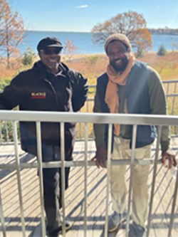 Two African American men stand infront of a blue body of water.