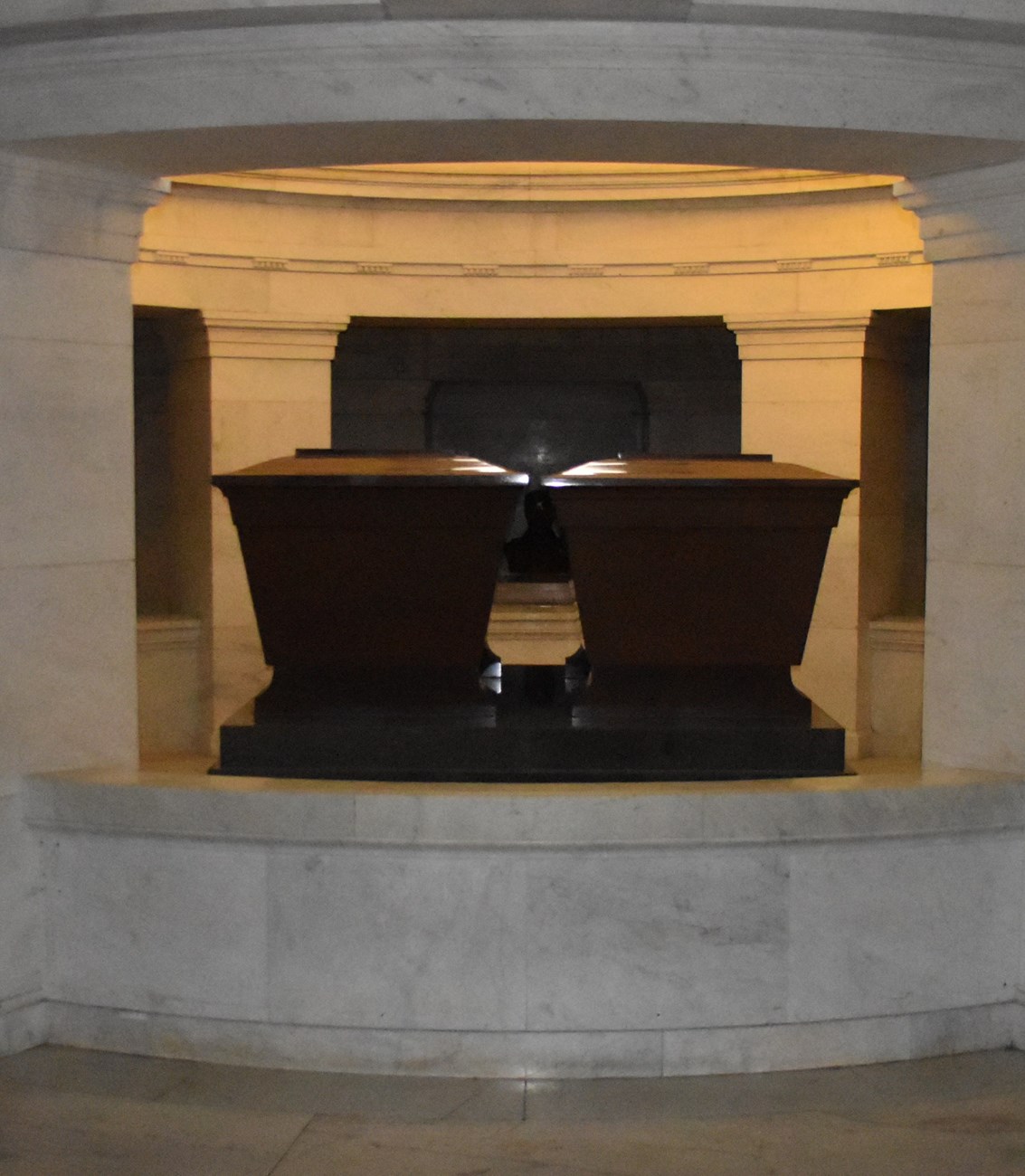 Two dark sarcophagi next to one another on the base layer of a white granite crypt
