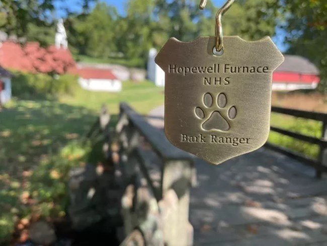 B.A.R.K. Ranger badge in front of Hopewell Village. NPS/Vidrio-Toews