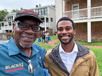 Two African American men take a selfie infront of buildings.
